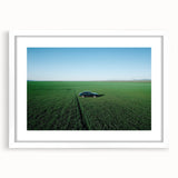 Framed landscape artwork showcasing a serene countryside scene, featuring vibrant greens and soft blues, presented in a sleek white mat and frame for an elegant display.