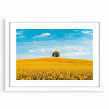 Framed landscape print depicting serene countryside scenery with lush green fields and a clear blue sky, finished with a white mat for an elegant look.