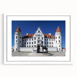 Elegant white-framed artwork showcasing a scenic landscape with a majestic castle under a clear blue sky, ideal for home decor or office settings.