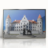 Framed acrylic artwork depicting a serene landscape with a castle surrounded by lush greenery and a clear blue sky, featuring elegant silver accents for a sophisticated finish.