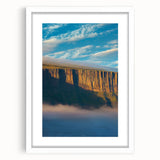 Framed landscape artwork showcasing majestic cliffs under a clear blue sky, surrounded by a white mat, perfect for home decor or office enhancement.
