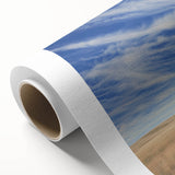 Rolled canvas displaying a vibrant landscape scene of a rustic barn under a clear blue sky, packaged in a protective cardboard tube for safe delivery.