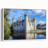 Framed canvas artwork depicting a serene landscape with a majestic castle surrounded by lush greenery, featuring a white frame that enhances the visual appeal. Perfect for home decor enthusiasts seeking to elevate their interior design with classic elegance.