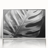 Framed botanical wall art featuring a vibrant Monstera leaf design in a sleek white frame, showcasing lush green hues and intricate details, perfect for modern decor.
