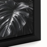 Close-up of a framed botanical wall art featuring a vibrant monstera leaf design on textured canvas, ideal for adding a tropical touch to home decor.