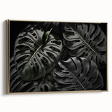 Framed canvas wall art showcasing a botanical monstera design with vibrant green leaves, elegantly displayed with a gold frame against a neutral background.