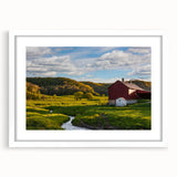 Framed wall art featuring a serene landscape of rustic barns, surrounded by lush greenery and soft clouds, presented in a white mat for an elegant finish.