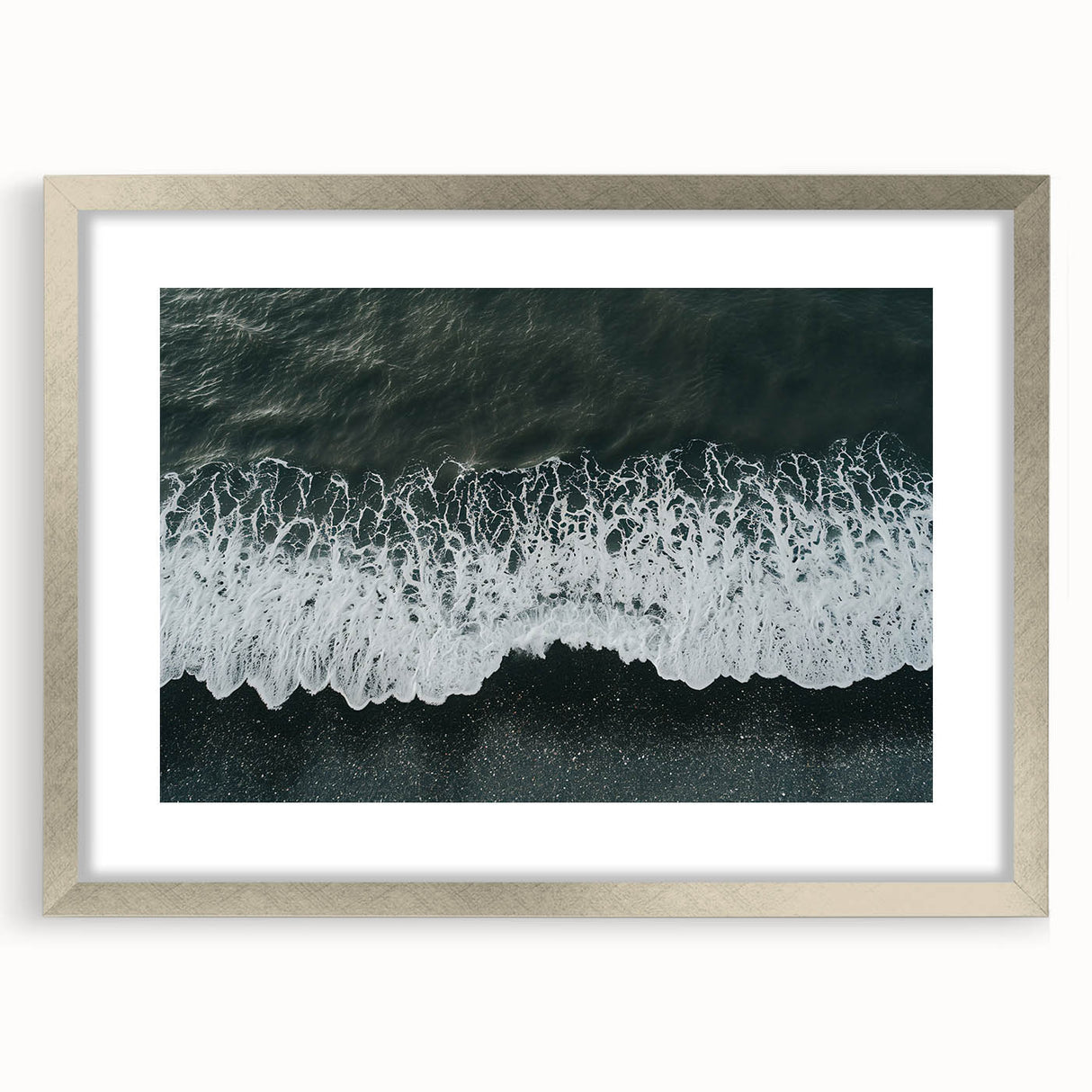 Framed wall art featuring a serene beach landscape with soft waves and golden sand, surrounded by a silver mat, ideal for coastal home decor.