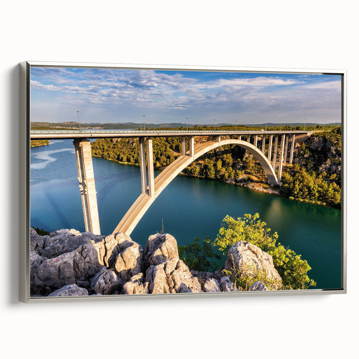 Framed canvas wall art depicting a serene landscape with a bridge, featuring a silver frame and vibrant colors, perfect for home decor or office space enhancement. This art piece adds a touch of elegance and tranquility to any room, making it an ideal choice for nature lovers and art enthusiasts.