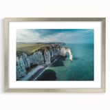 Framed wall art featuring a serene landscape of cliffs and mountains, with a silver frame and mat, adding elegance to any home decor setting.