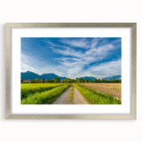 Framed wall art showcasing a serene countryside landscape with vibrant greens and soft blues, elegantly designed with a silver mat and frame, perfect for home decor.