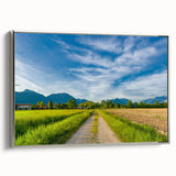 Framed canvas wall art depicting a serene countryside landscape, featuring lush green fields and distant mountains, presented in a sleek silver frame for a modern touch.