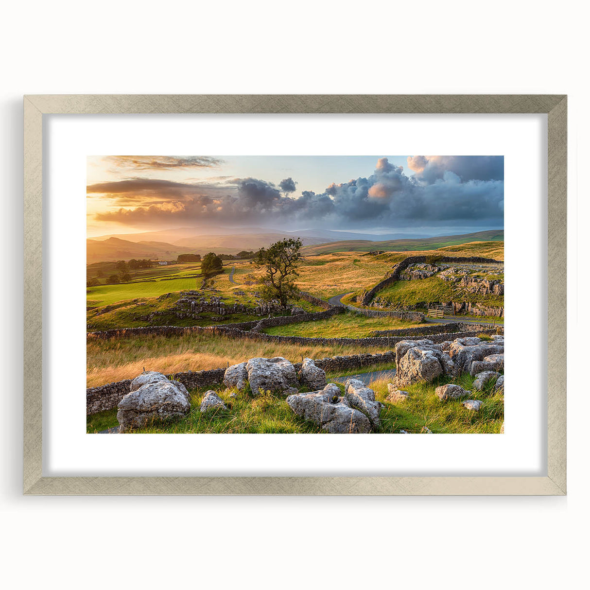 Framed wall art showcasing a serene countryside landscape, featuring vibrant green fields, a clear blue sky, and delicate white clouds, presented in a sleek silver frame with a mat for an elegant display.