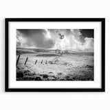 Framed landscape wall art featuring a serene countryside scene with vibrant green fields and a bright blue sky, encased in a stylish black frame with a mat.