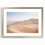 Framed desert landscape wall art featuring warm tones of orange and beige, showcasing a serene sunset over sand dunes, with a sleek silver mat and frame. Perfect for modern home decor.