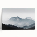 Stretched canvas wall art featuring a serene misty landscape design with soft gray and green tones, leaning against a textured wall, perfect for home decor.
