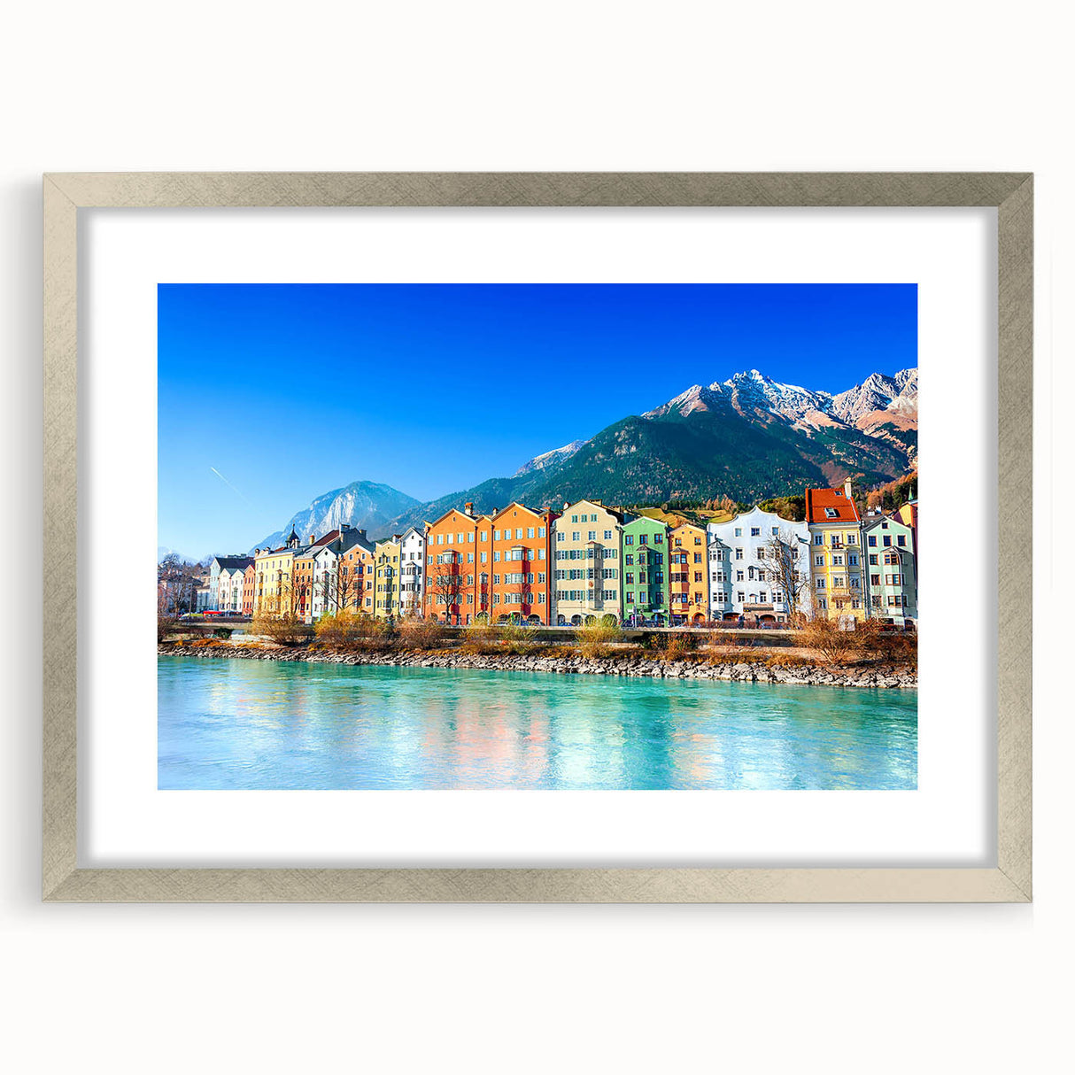 Framed wall art depicting a serene village landscape with vibrant colors, set in a sleek silver frame with a mat for an elegant display, perfect for home decor.