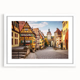 Framed landscape wall art showcasing a serene village scene, featuring vibrant colors and intricate details, set in a white mat for an elegant presentation.