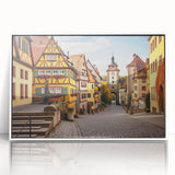 Framed wall art showcasing a picturesque village landscape design in vibrant colors, displayed in a sleek white frame, perfect for home decor.