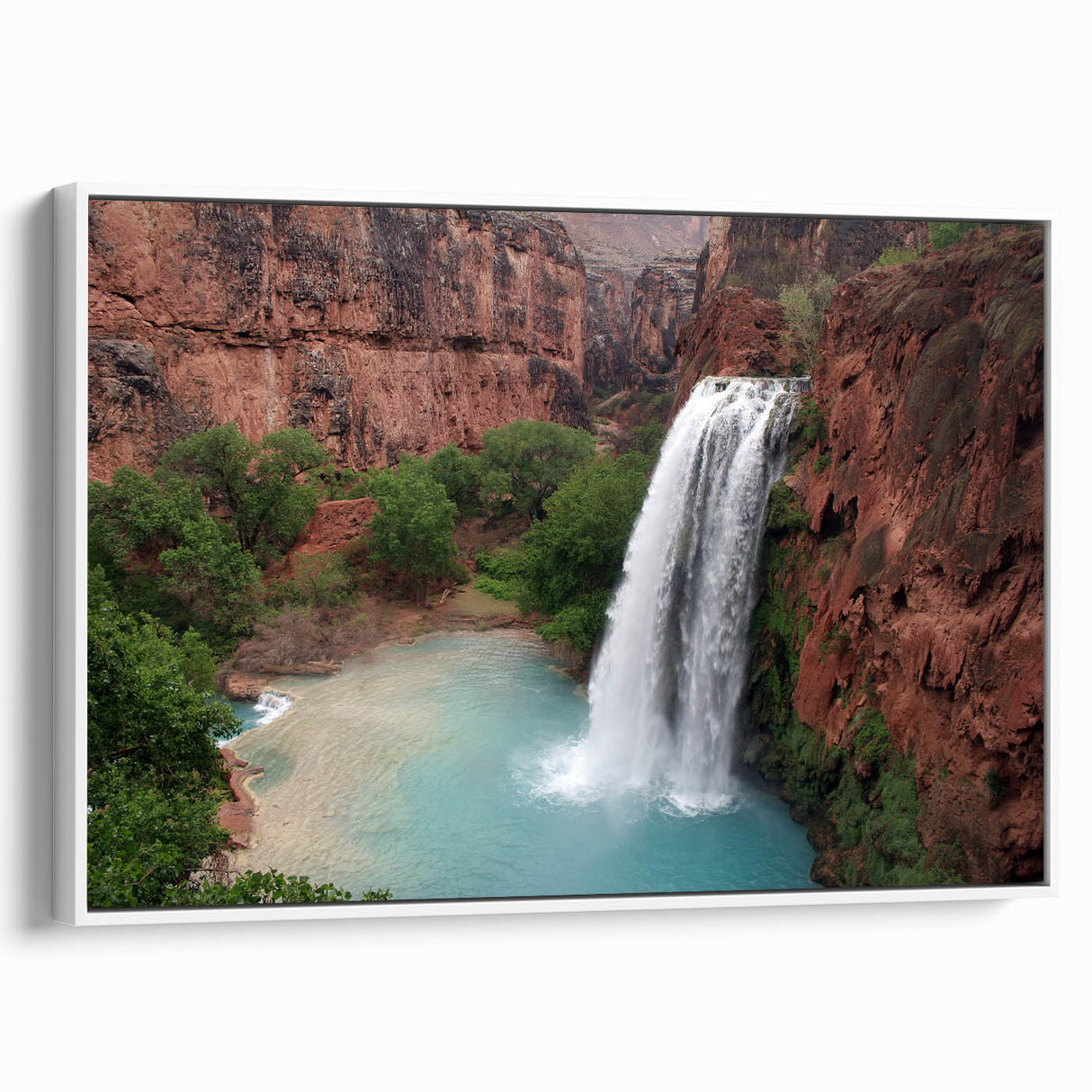 Framed canvas wall art showcasing a serene waterfall landscape, featuring vibrant blues and greens, elegantly displayed with a white frame, perfect for home decor.