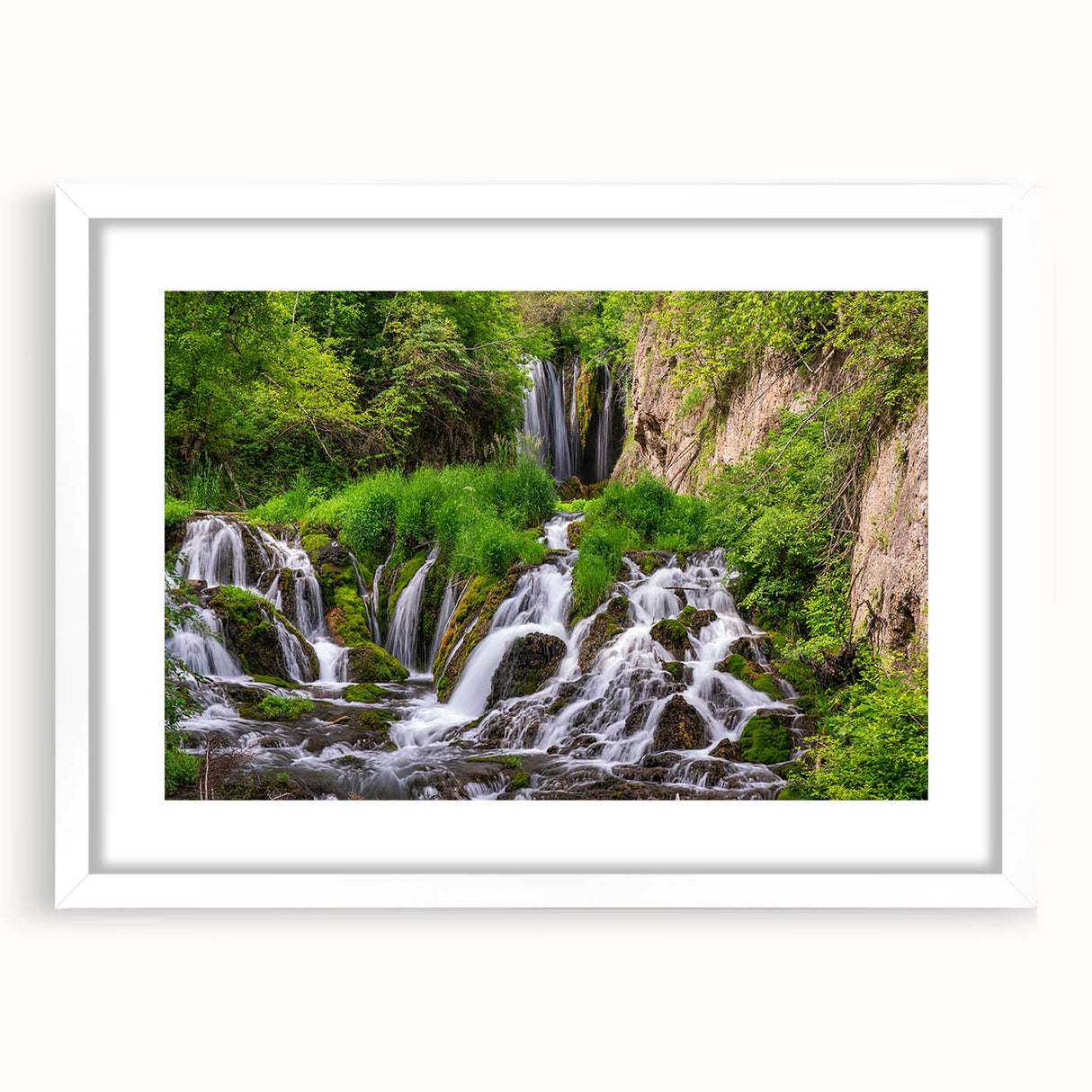 Framed wall art featuring a serene landscape of cascading waterfalls, surrounded by lush greenery, with a white mat and frame for an elegant display. Ideal for home decor.