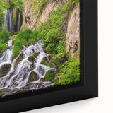 Close-up of a framed canvas artwork depicting a vibrant waterfall landscape, showcasing rich blues and greens, perfect for enhancing home decor with nature's beauty.