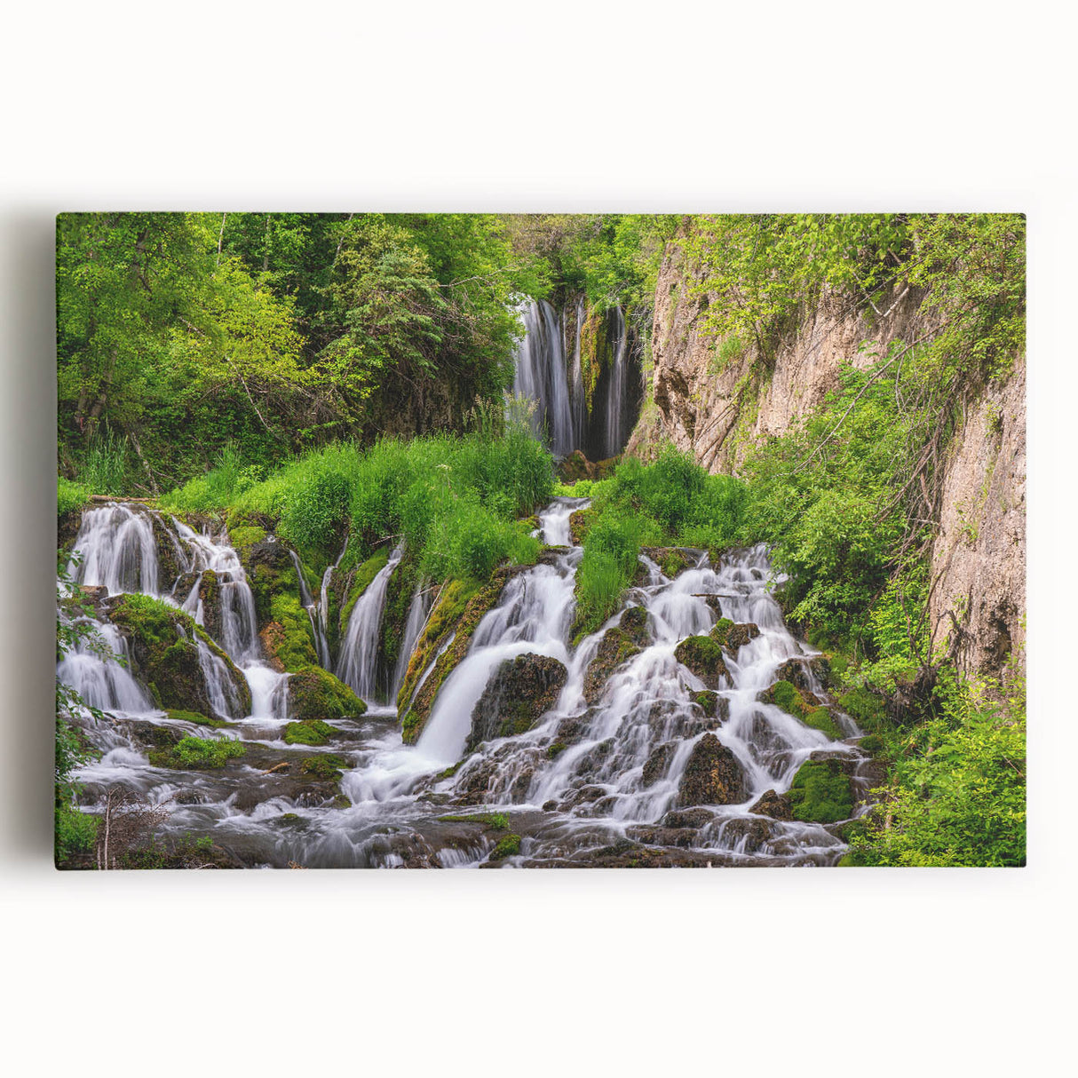 Stretched canvas wall art depicting a serene waterfall landscape, showcasing vibrant greens and soothing blues, perfect for enhancing home decor with a natural theme.