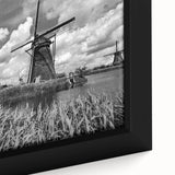 Close-up of a framed canvas wall art piece depicting a serene landscape with windmills under a cloudy sky, showcasing vibrant colors and intricate details. This artwork enhances home decor with a touch of tranquility and nature-inspired beauty.