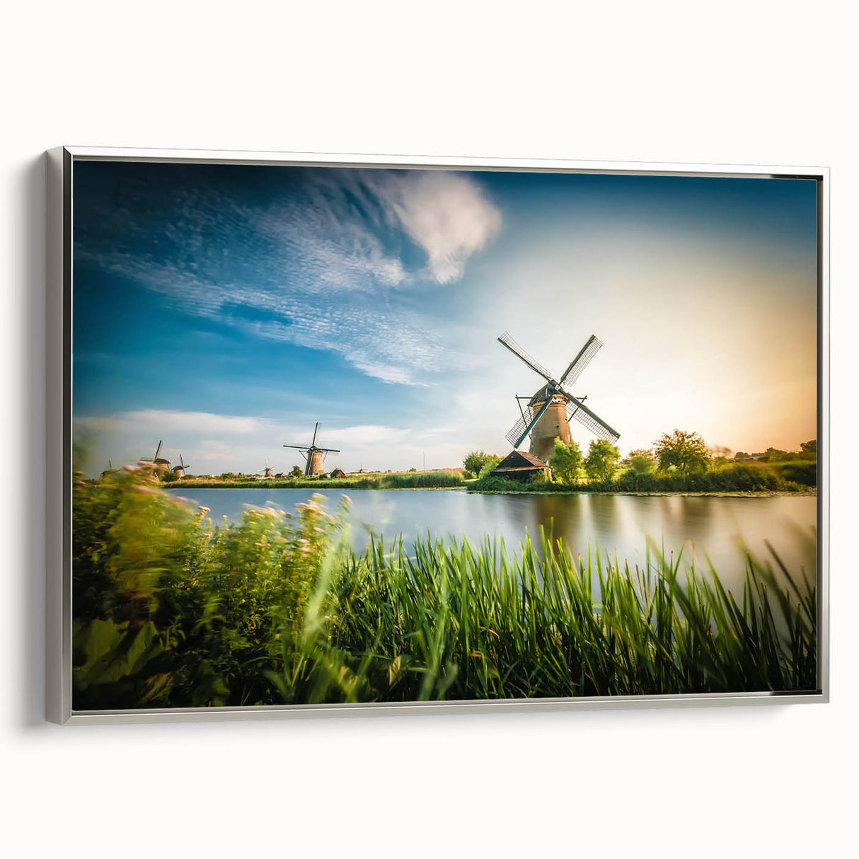 Framed canvas artwork depicting a serene landscape with windmills under a vibrant sunset, featuring silver accents and a sleek side profile for modern decor. Perfect for enhancing home aesthetics.