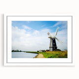 Framed wall art depicting a serene landscape with windmills, featuring a white mat and sleek frame, ideal for home decor and enhancing interior aesthetics.