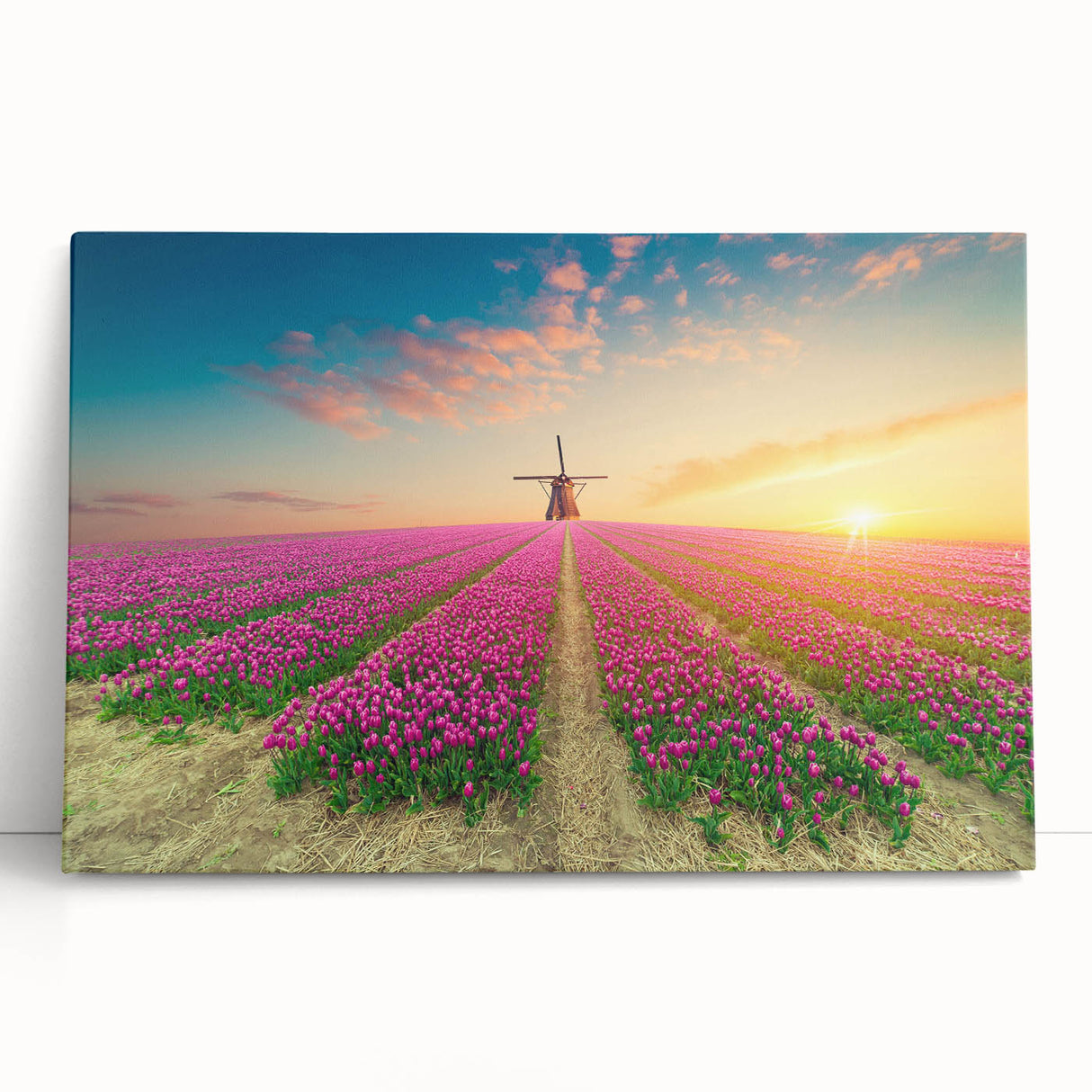 Stretched canvas wall art showcasing a serene landscape of windmills against a vibrant sunset, leaning against a textured wall. Ideal for home decor enthusiasts.