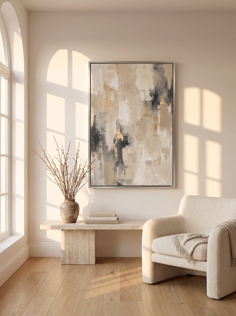 Framed canvas print of a greige and gold abstract in a silver floater frame above a travertine bench