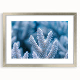Abstract art print featuring frost-inspired patterns in pale blue and white tones, framed in silver.