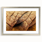 Textured art depicting abstract leaf designs in green and gold on a silver-framed mat, suitable for bedroom decor.