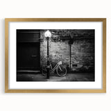 Abstract art print of a bicycle silhouette in gold and black tones, framed with a mat, suitable for dining room decor.