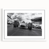Abstract art print of race cars in motion, using bold red and blue tones on a white framed canvas.